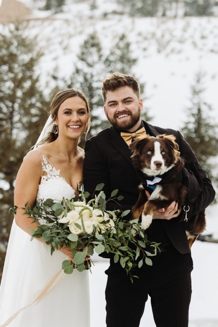A bride and groom holding their dog in the snow.