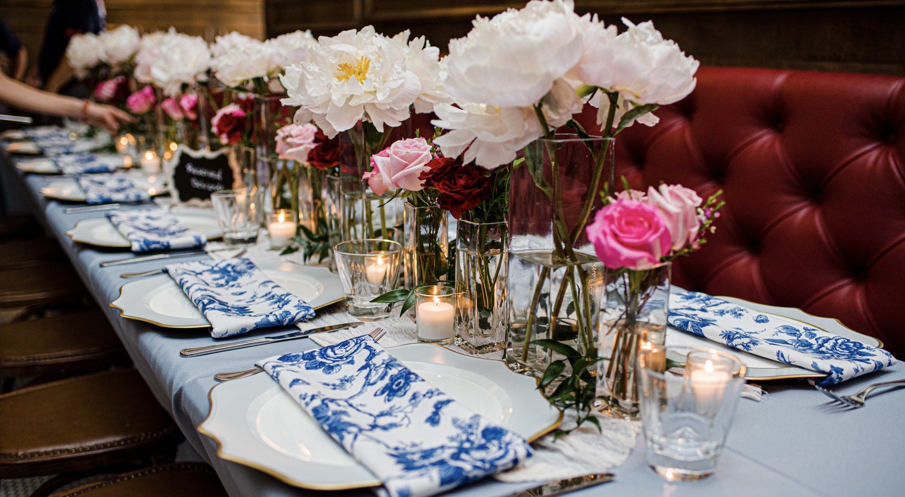 A table set with plates and candles, flowers in vases.