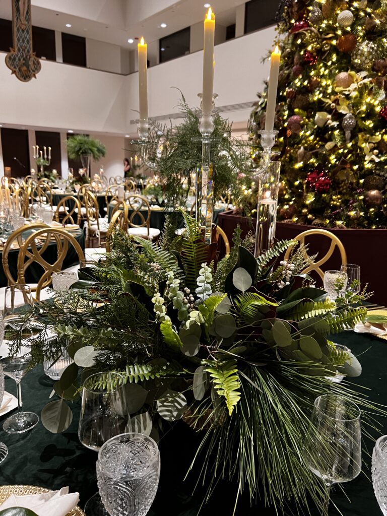 Elegant Christmas centerpiece with greenery and candles in a decorated dining area.