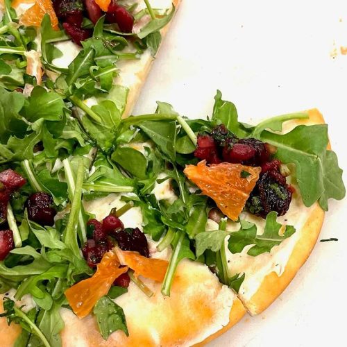 A fresh arugula and roasted vegetable flatbread pizza.