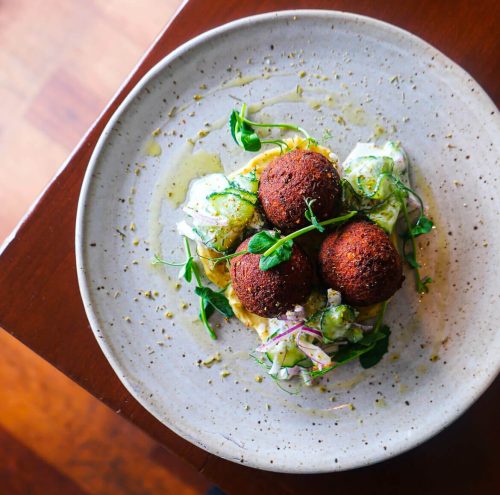 Plated falafel balls with fresh greens, drizzled sauce, and herbs.
