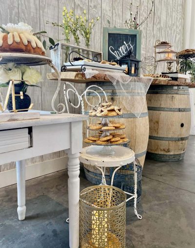A rustic bakery corner with pastries on a white chair and wooden barrels in the background.