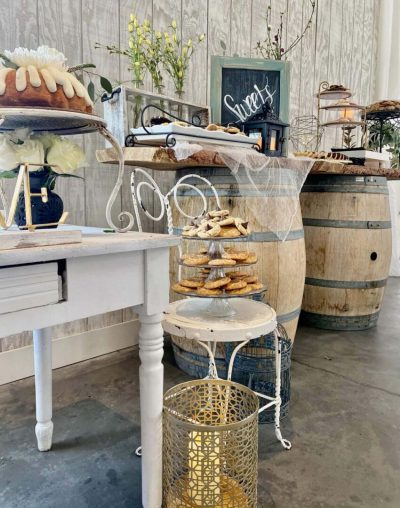 A rustic bakery corner with pastries on a white chair and wooden barrels in the background.